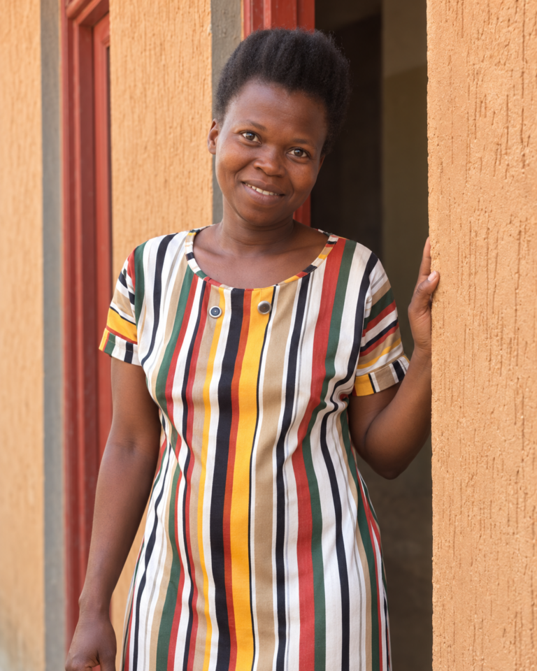 Consolatte Bucumi smiles in a school doorway, wearing a colorful striped dress.